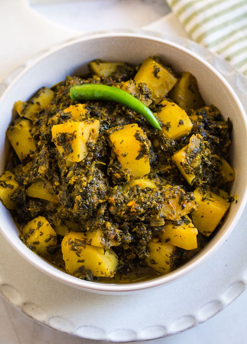 Overhead shot of aloo palak in a white bowl, topped with a whole green chili.