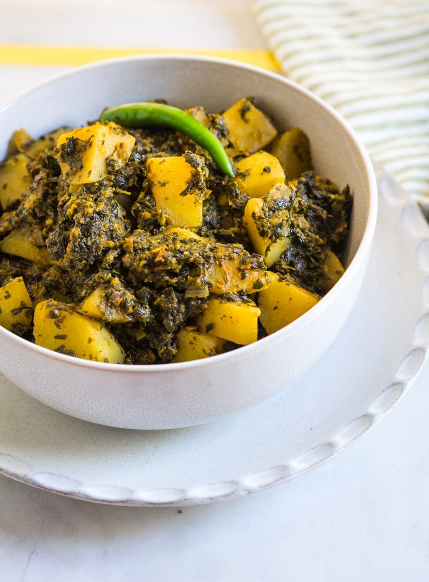 Aloo Palak served in a white bowl, placed on top of a white plate.