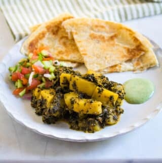 A plate of aloo palak with paratha, kachumber, and mint raita.