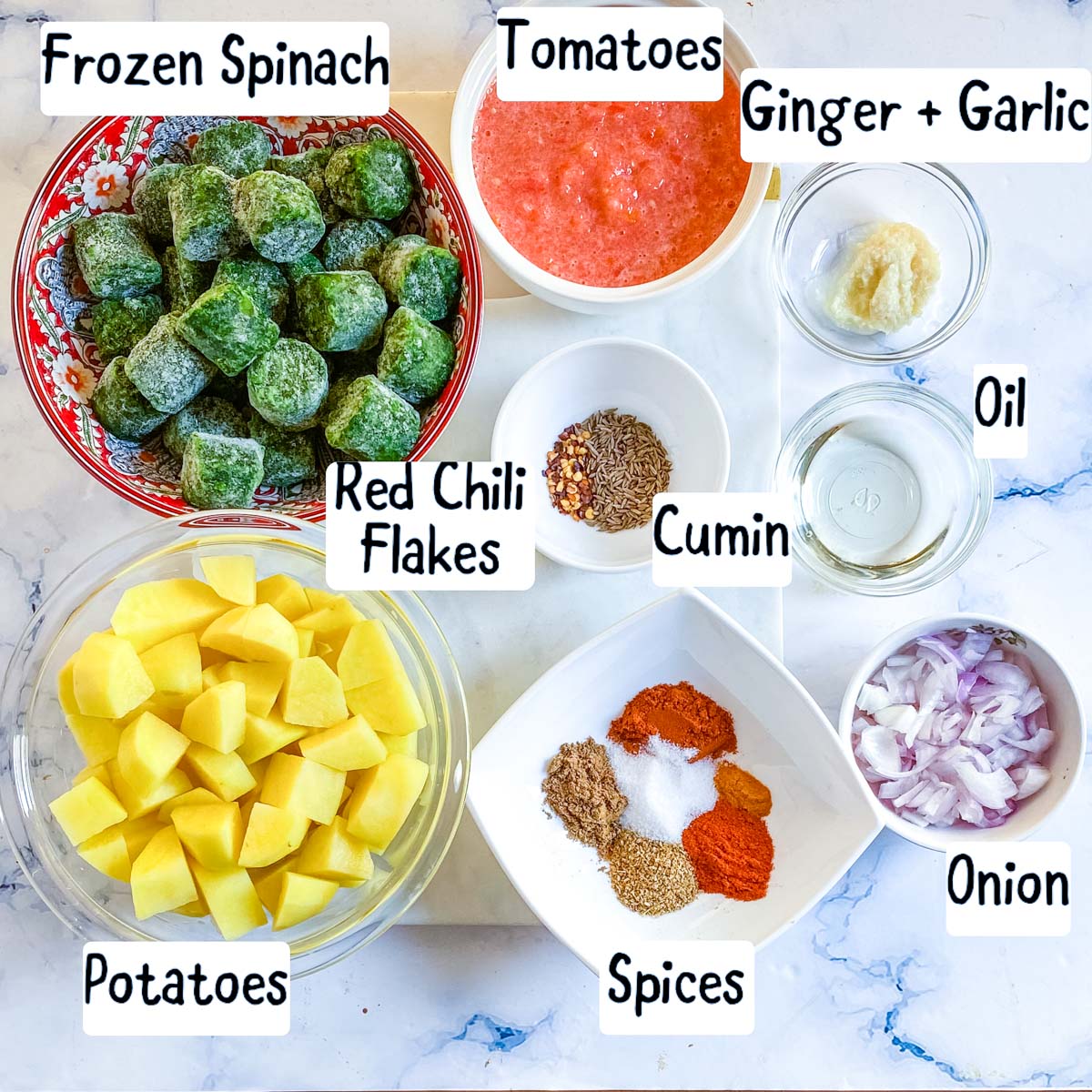 Ingredients to make palak aloo laid out on a white marble backdrop.