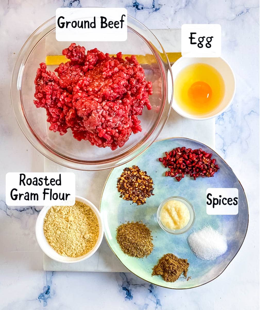 Ground beef, egg, spices, and roasted gram flour laid out on a white marble slab.