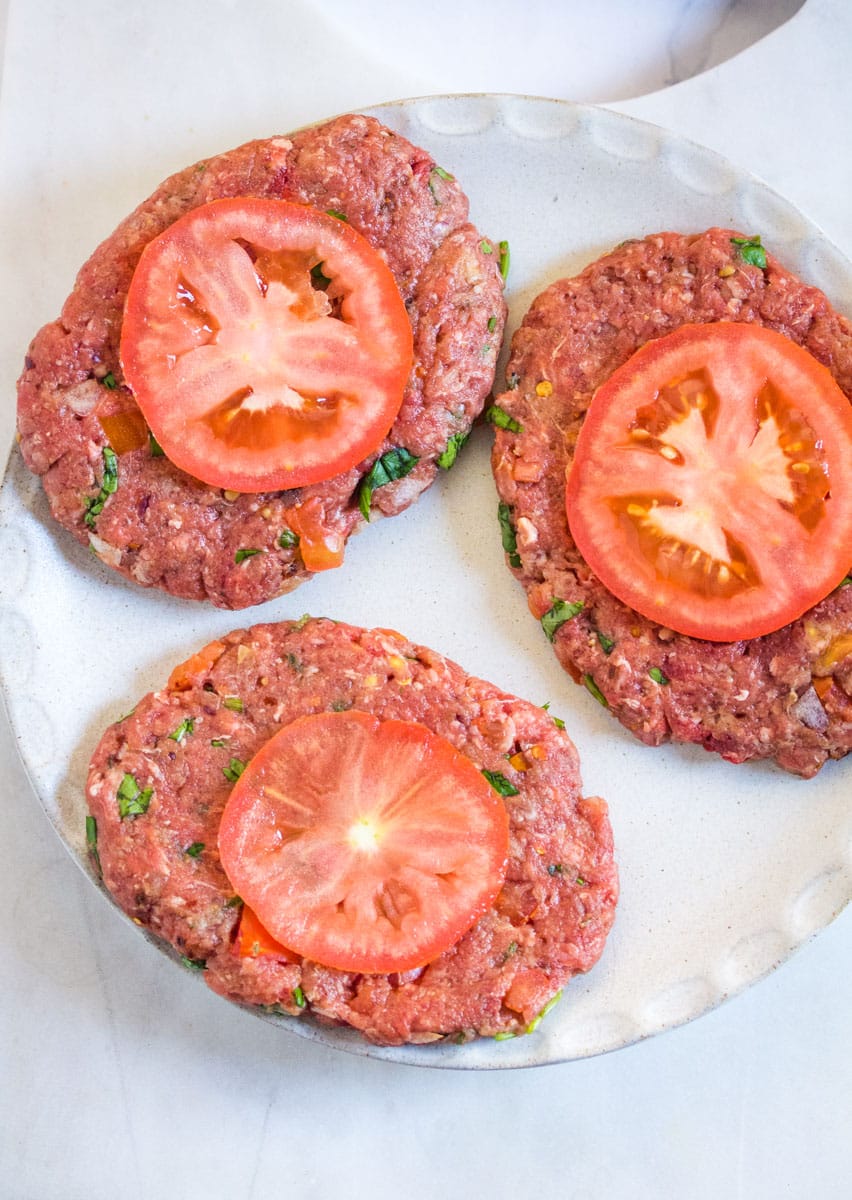 A plate of raw chapli kabab topped with fresh tomato slices.