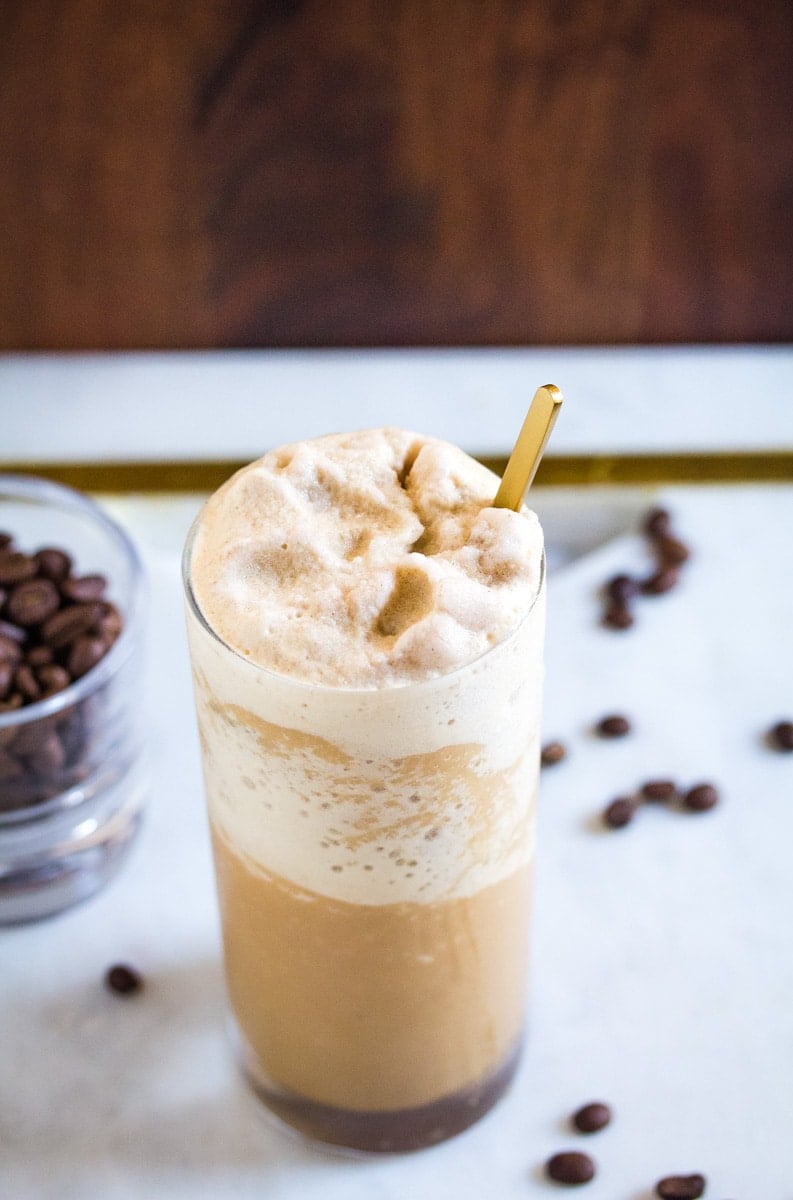 A top down shot of coffee slushie in a tall glass with scattered coffee beans around it.