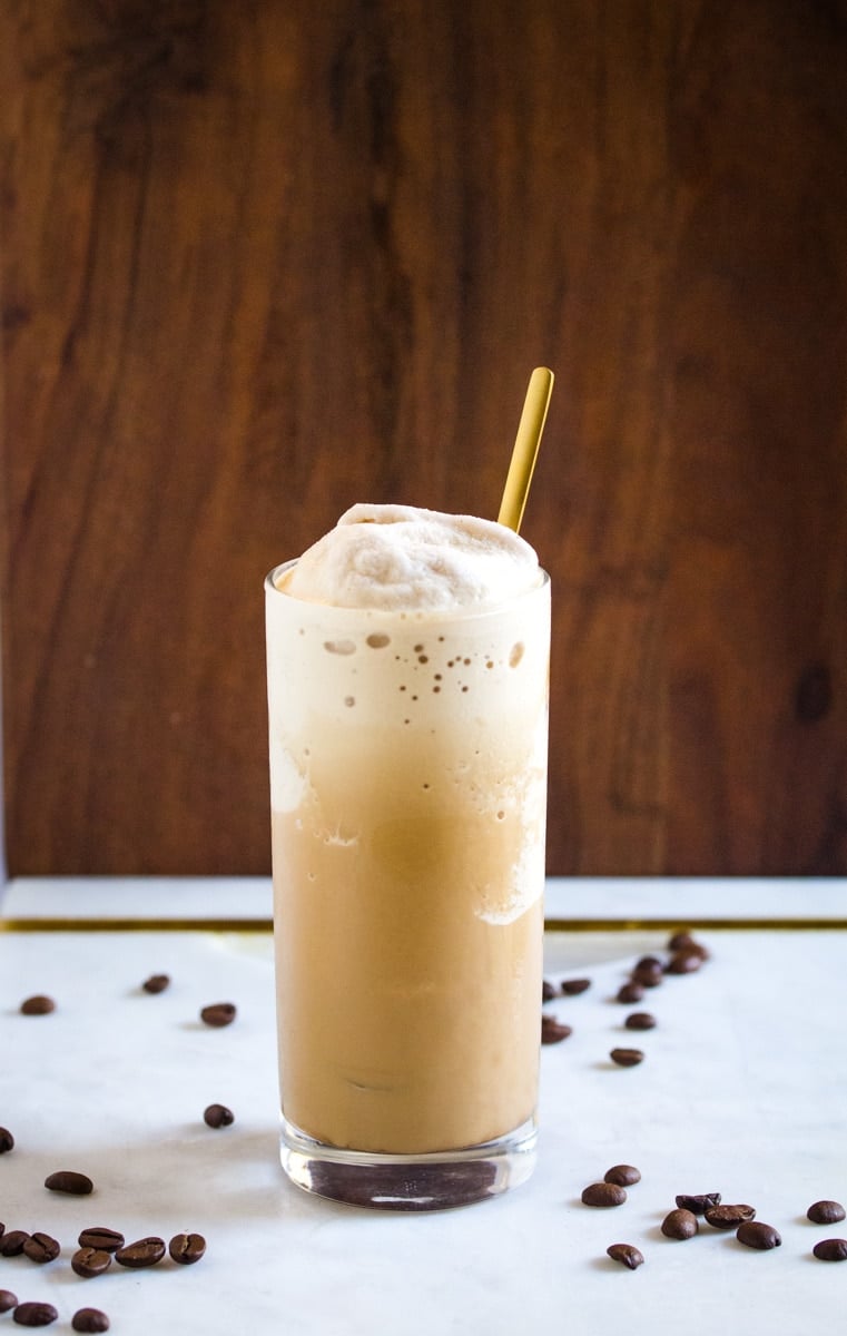 Coffee slush served in a tall glass with a gold spoon, placed on a white marble slab. 