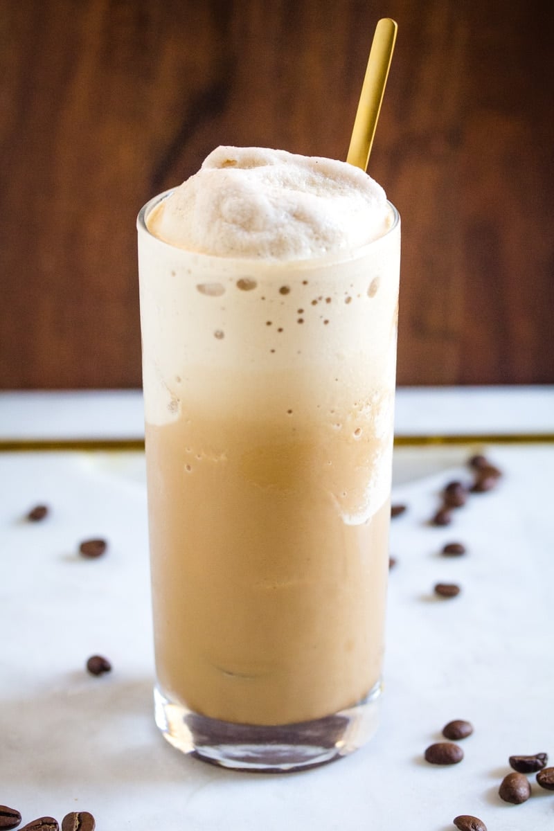 Close up shot of coffee slush in a tall, clear glass with a gold spoon sticking out.