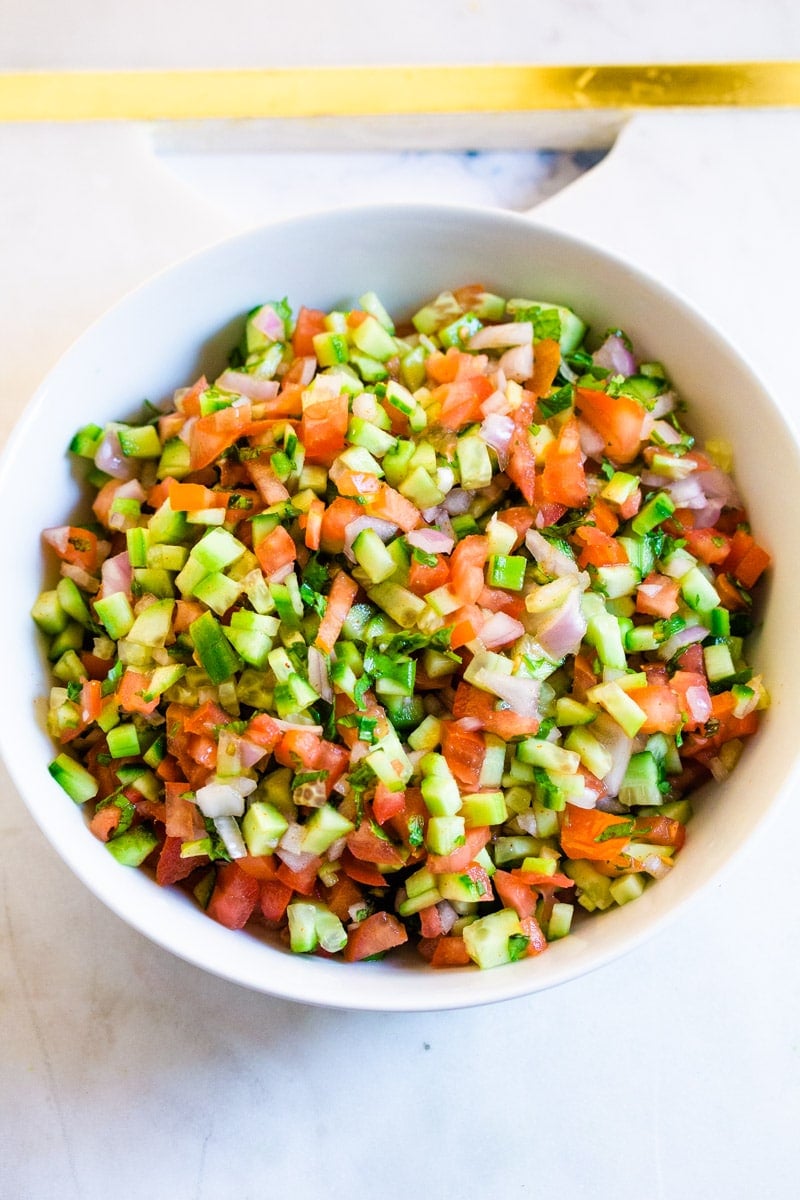 An overhead shot of Indian Salad served in a white bowl placed upon a white marble slab.