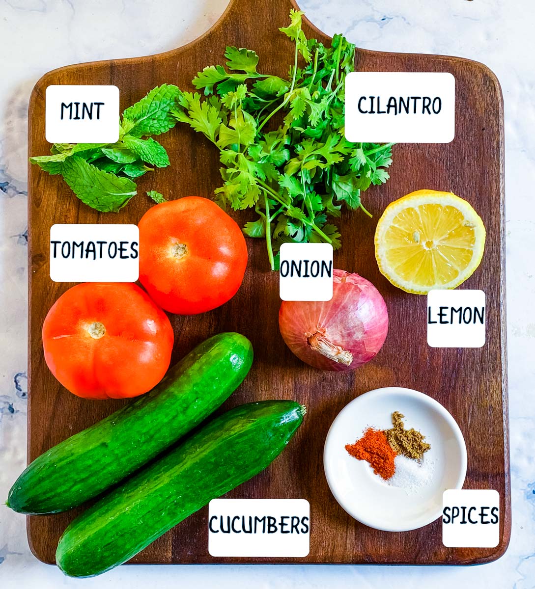 Ingredients for kachumber salad laid out on a brown wooden cutting board.
