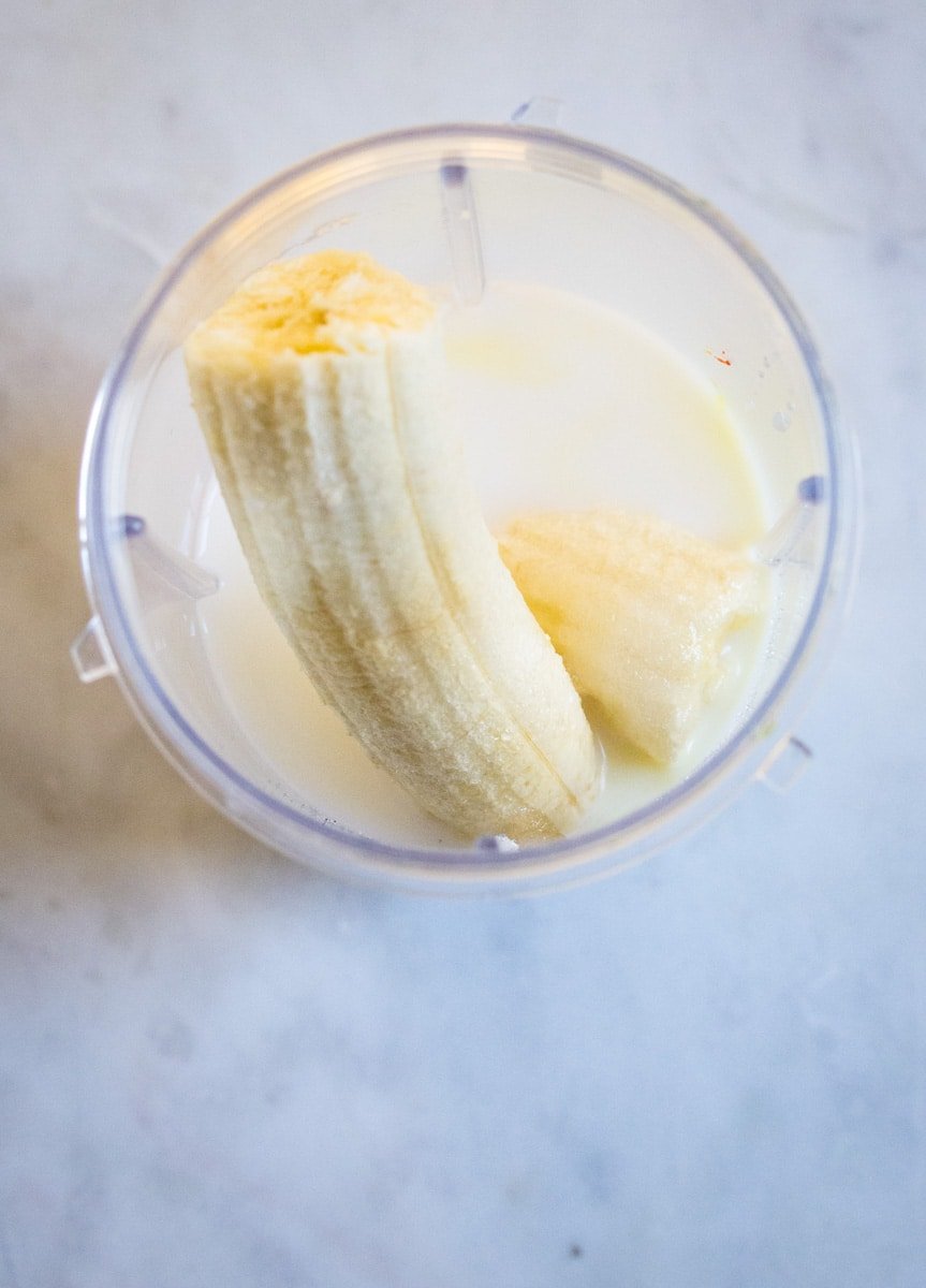 Chopped banana and milk placed in a blender on a white marble slab.