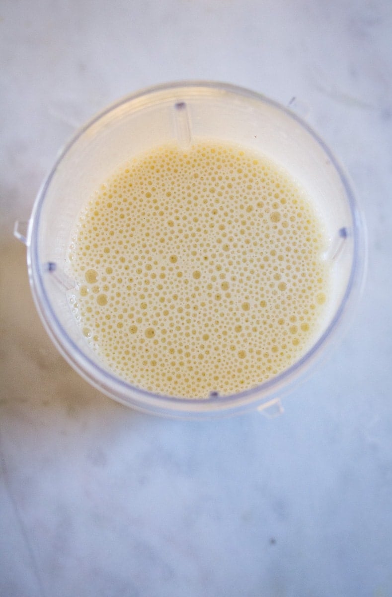 Blended banana milk in a blender placed on a white marble slab.