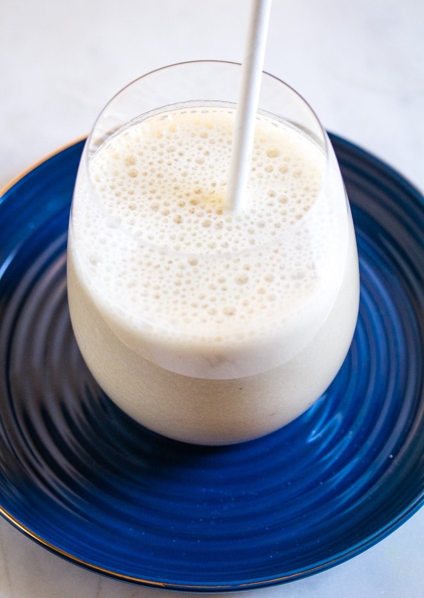 Korean Banana Milk pictured in a glass placed on a dark blue plate.