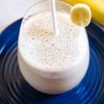 A glass of Korean banana milk on a dark blue plate with a white straw.