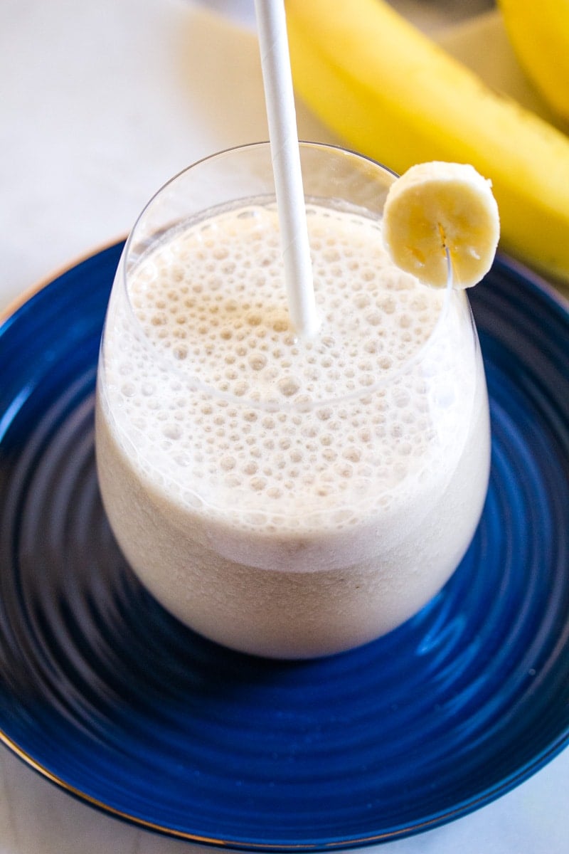 A glass of Korean banana milk on a dark blue plate with a white straw.