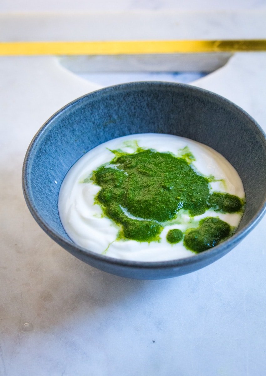 Plain yogurt topped with mint sauce in a dark grey bowl.