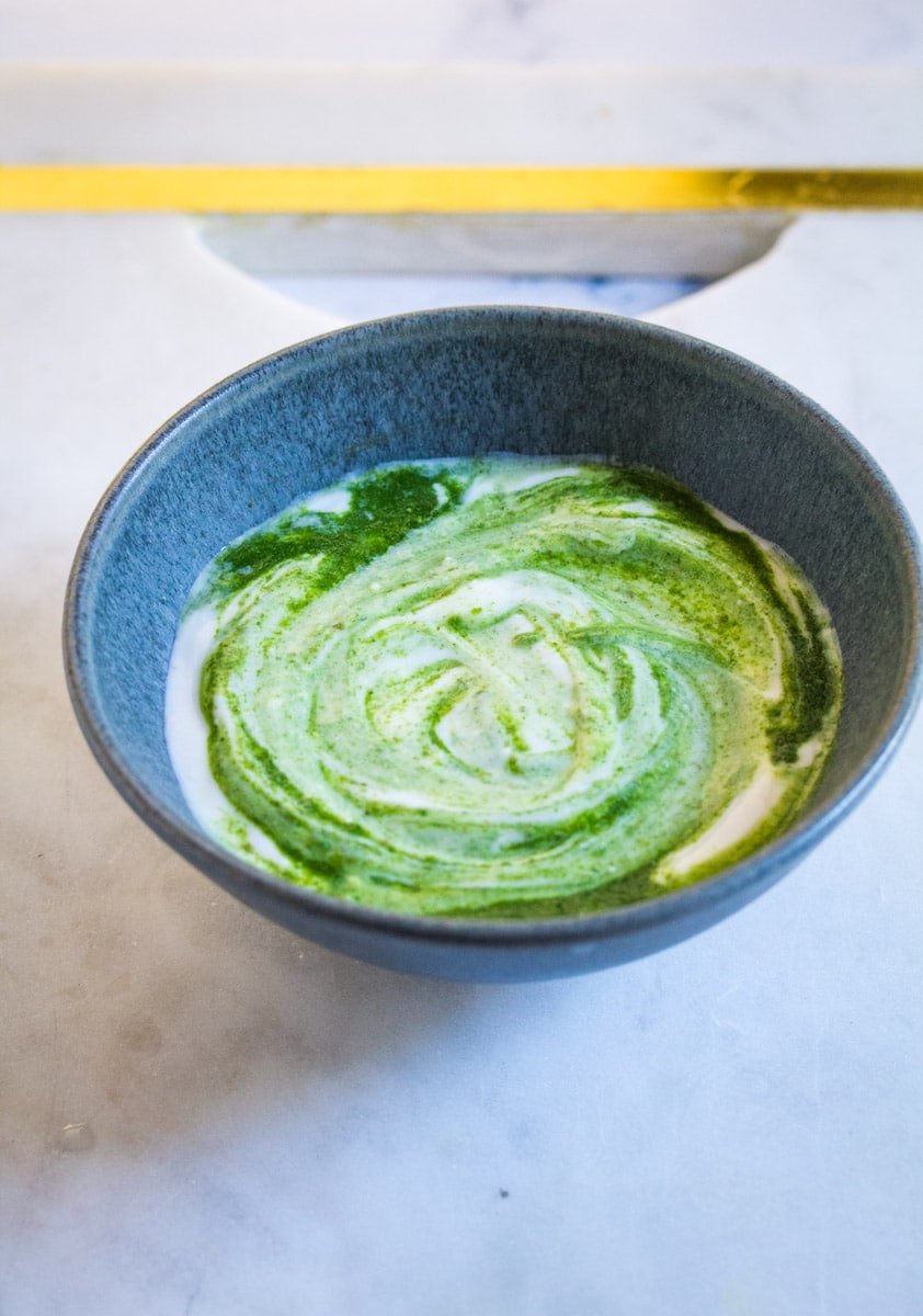 A bowl of yogurt with green mint sauce swirled in it.