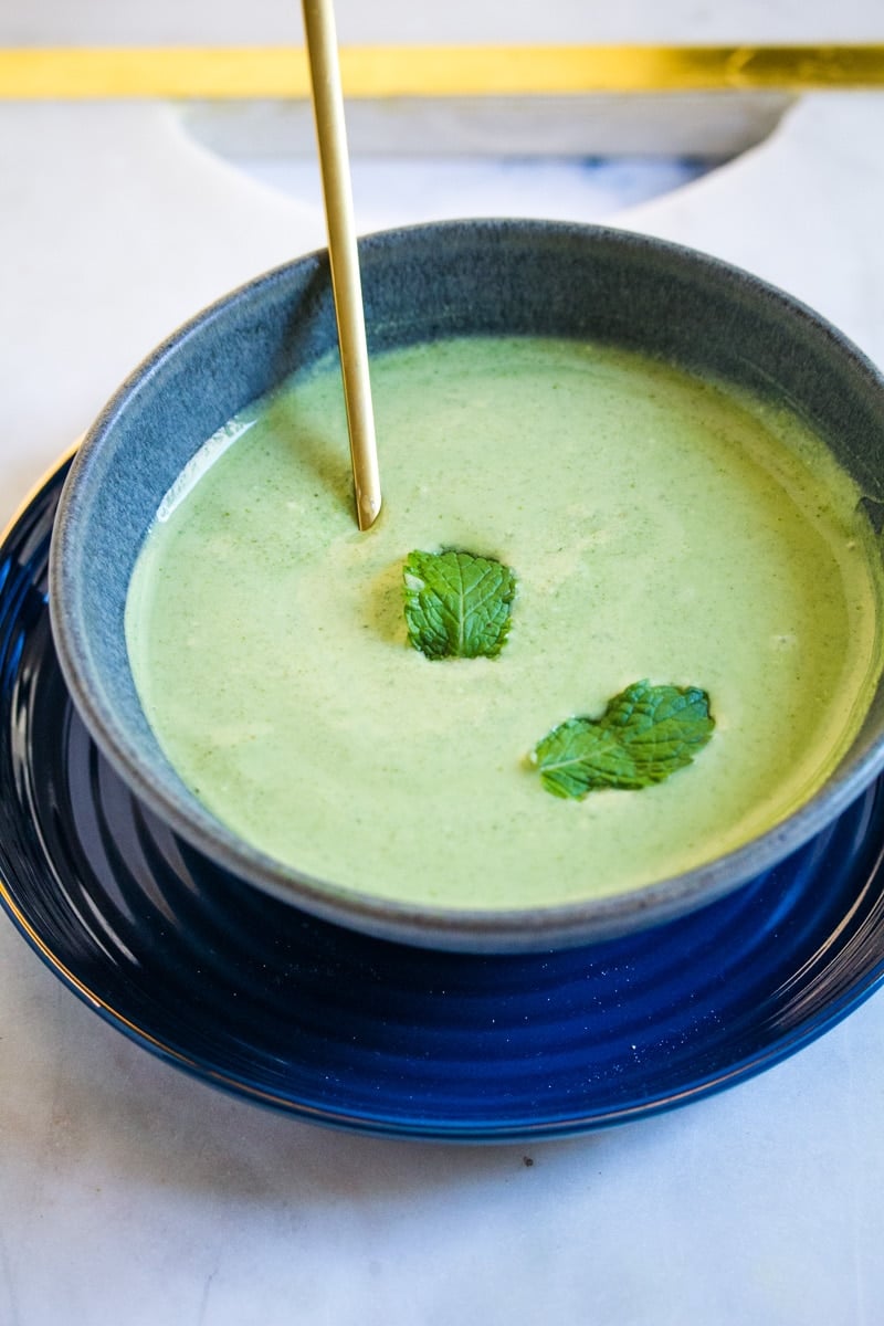 A picture of mint raita topped with two mint leaves, served in a grey bowl.