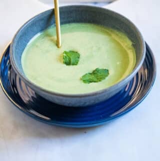 A bowl of mint raita served in a dark grey bowl, with a golden spoon.