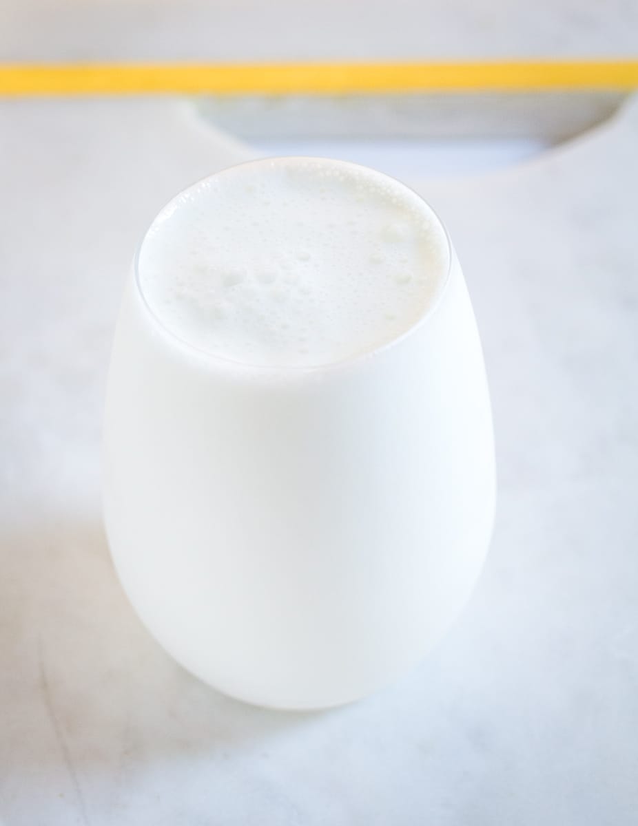 Lassi served in a round clear glass, placed on top of white marble slab.