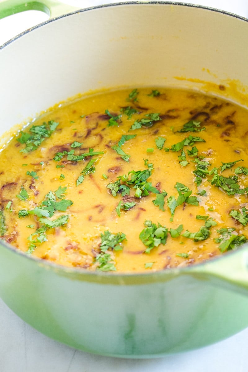 Cooked masoor dal in green dutch oven, topped with chopped cilantro and tempering.