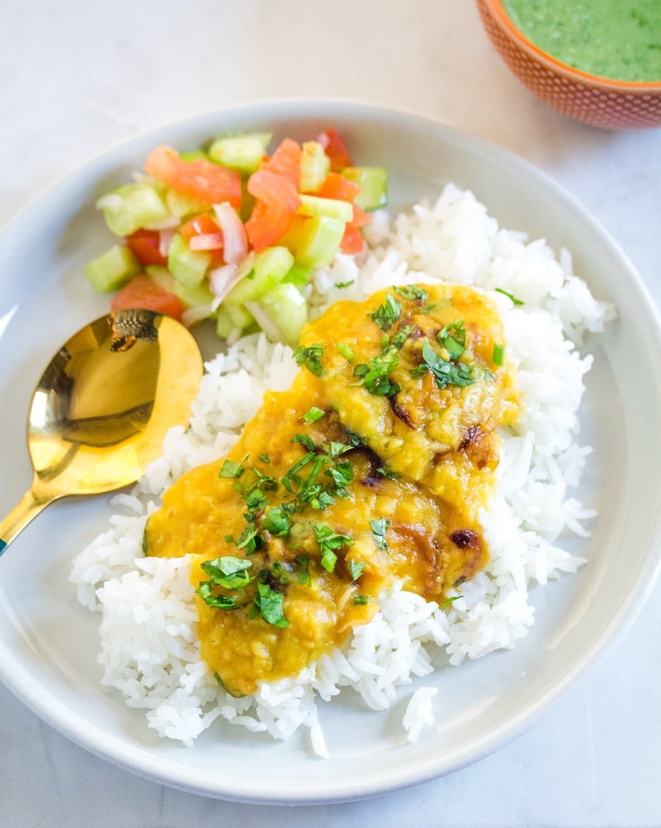 A plate of yellow daal served with white rice, kachumber salad and mint raita.