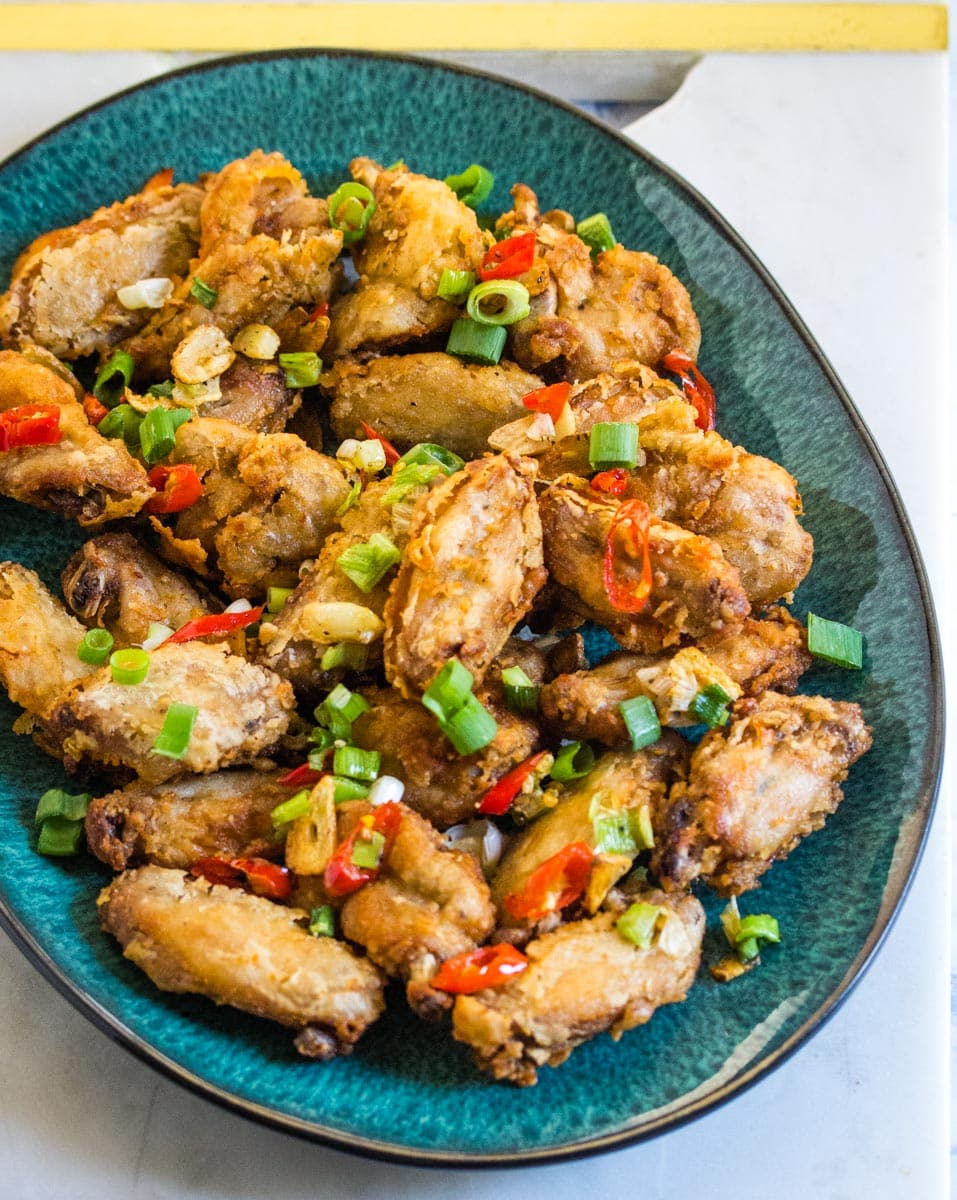 A close up shot of Chinese salt and pepper chicken wings served on a teal colored serving platter.