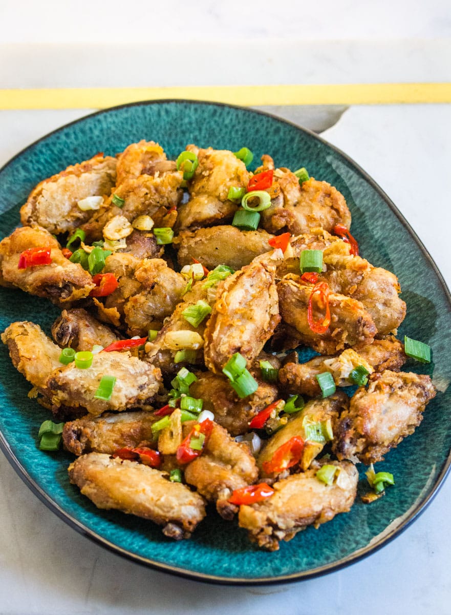 A teal colored platter of salt and pepper chicken wings topped with stir fried chilies and garlic.