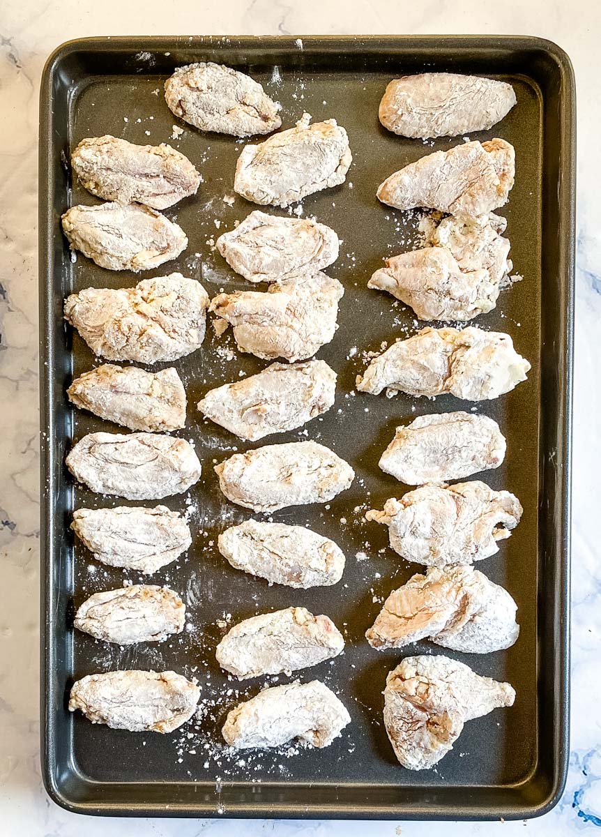 Chicken wings coated with a cornstarch dredge, lined up on a baking sheet.