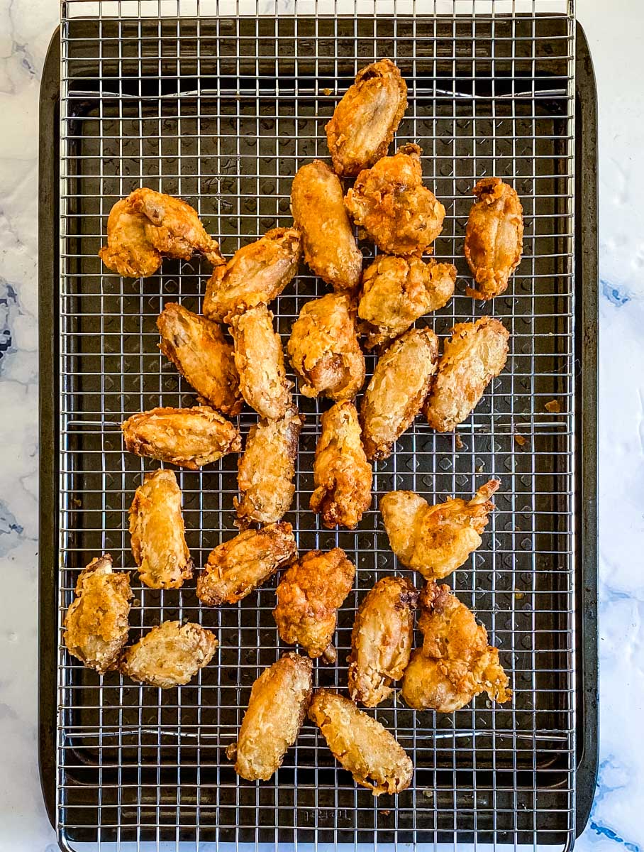 Deep fried chicken wings placed on a cooling wire rack.