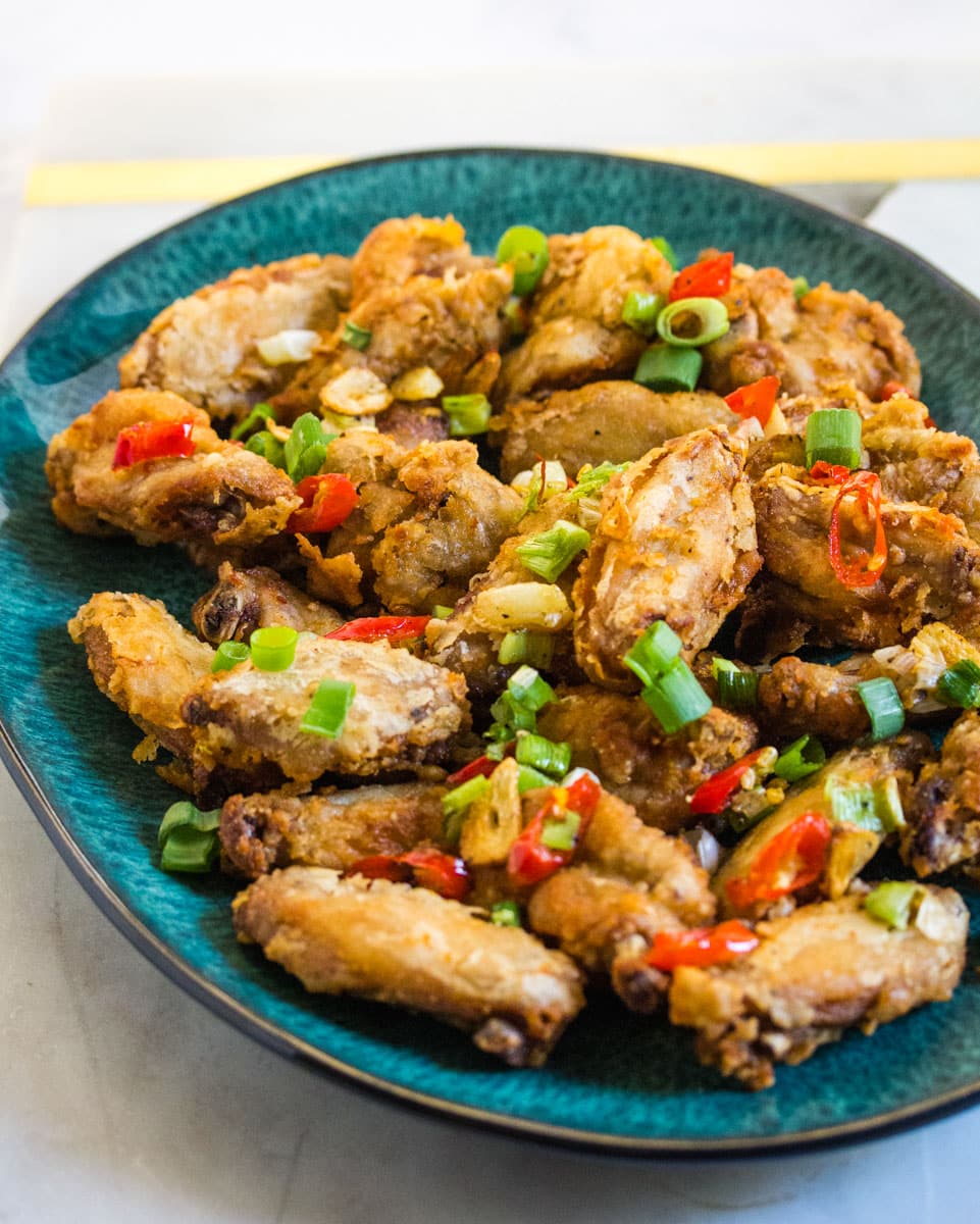 A plate of crispy fried chicken wings topped with chopped green onion and fried garlic. 