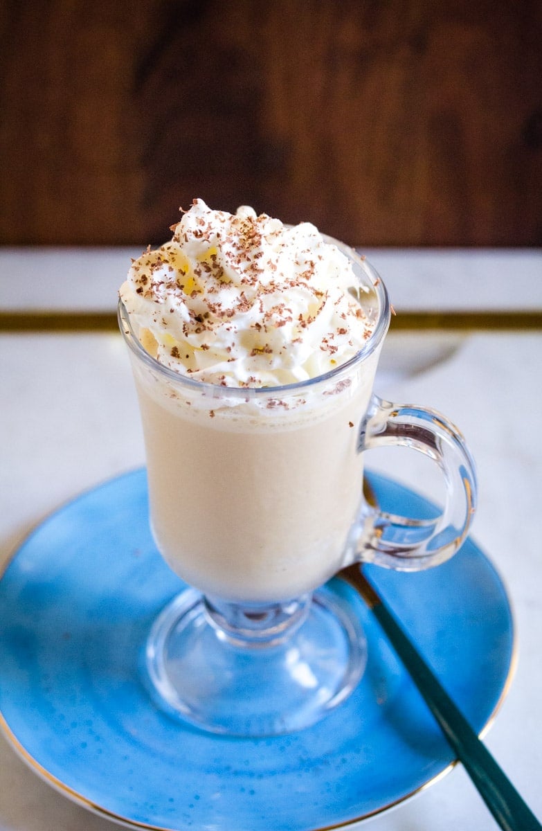 Coffee milkshake topped with whipped cream and chocolate shavings, served on a light blue plate.