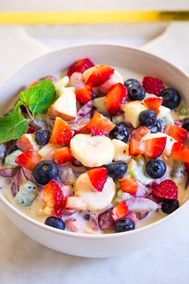 A light grey bowl filled with assorted and chopped fruit with a creamy sweet dressing.