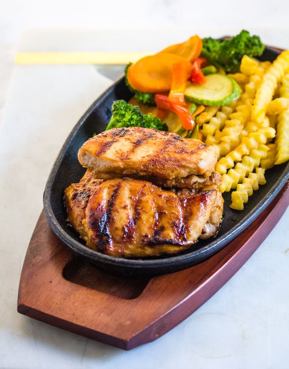 Grilled chicken steak served with sauteed vegetables and french fries on black plate