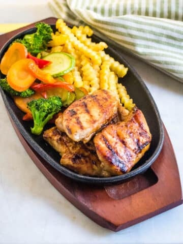 Grilled chicken steak served with sauteed vegetables and french fries on black plate