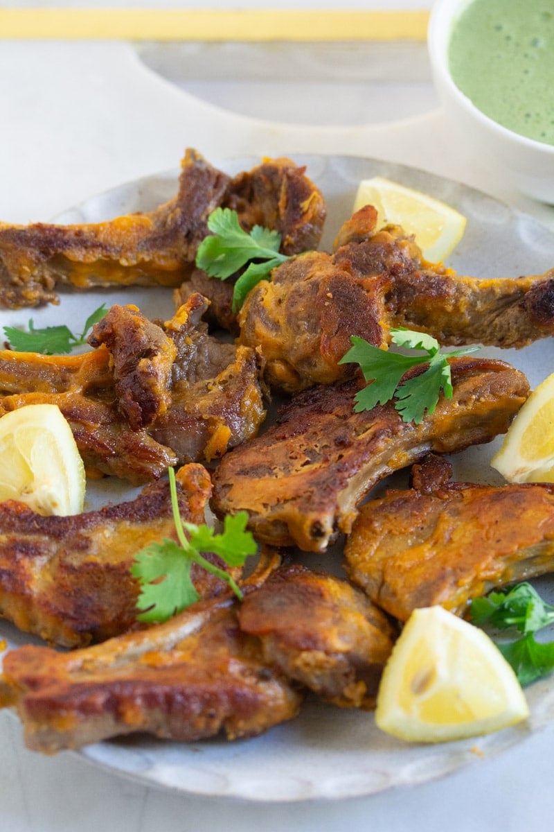 Close up shot of a plate of mutton chops garnished with coriander leaves and lemon wedges.