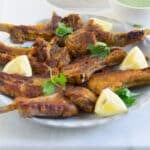 A plate of Pakistani mutton chaap fry garnished with lemon wedges and cilantro leaves.