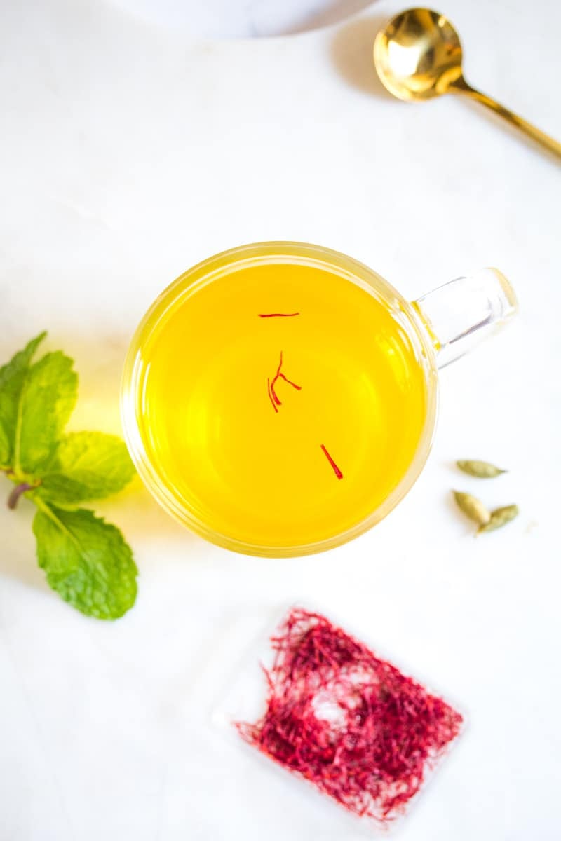 Overhead shot of saffron tea in a clear mug placed on a white marble slab.