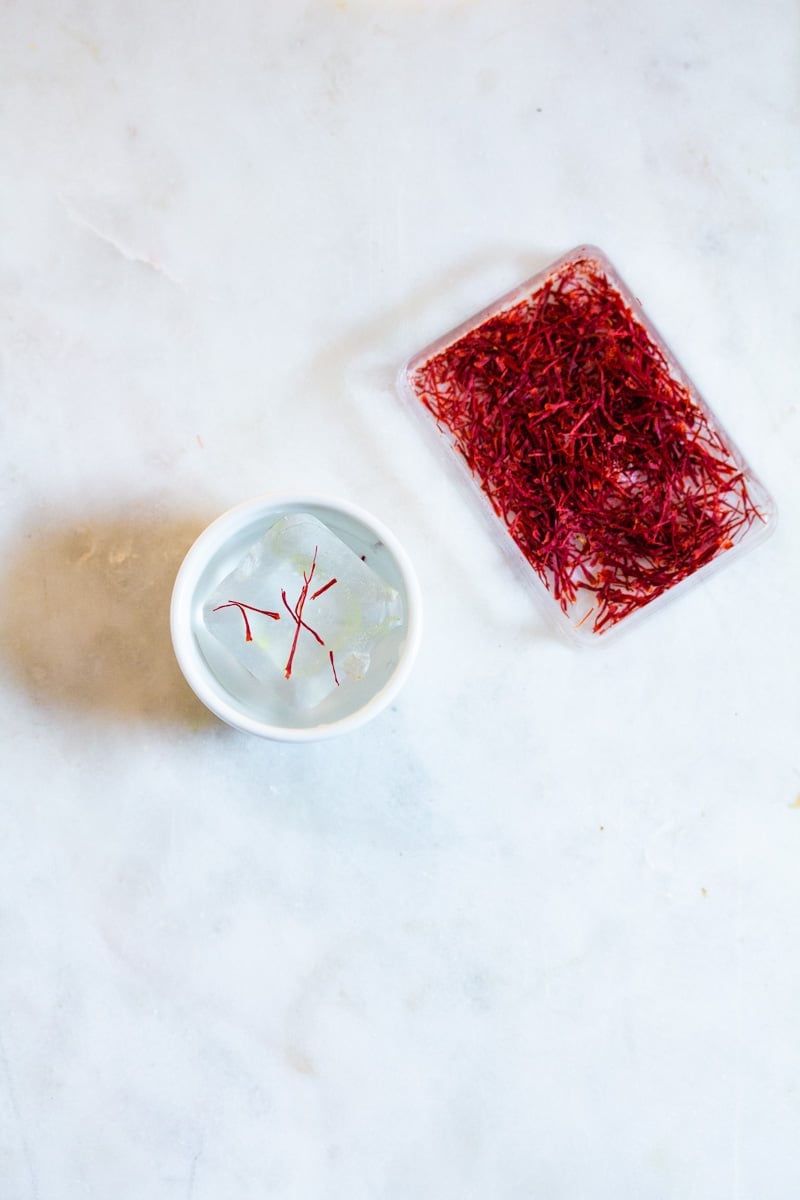 A box of saffron threads next to a small bowl with an ice cube.