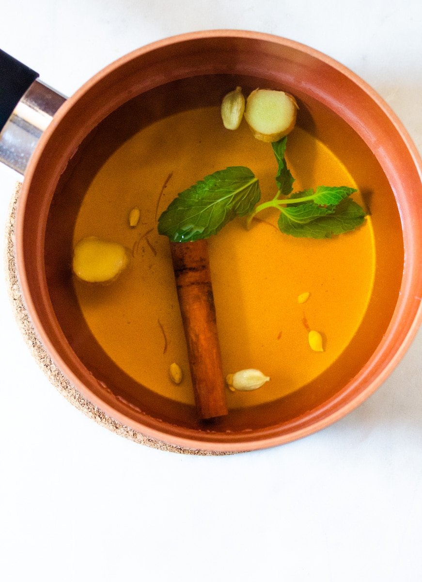 A pot of cooked saffron tea with ingreidents such as mint, sliced ginger, and cinnamon.