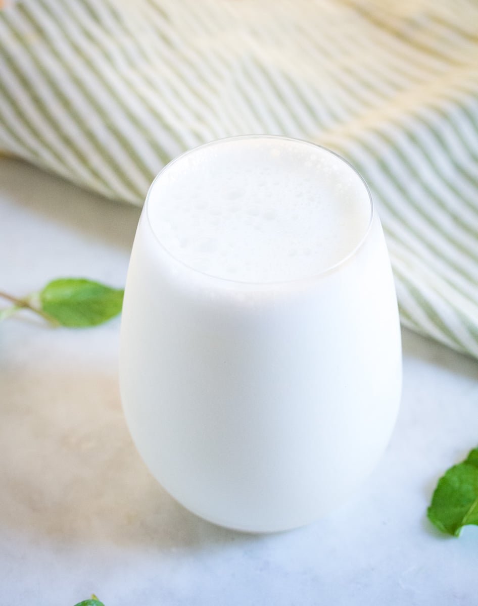 A glass of namkeen lassi served on a white marble slab, with two mint leaves scattered. 