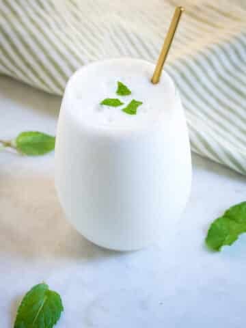 Salty lassi served in a glass goblet with a gold spoon and garnished with mint leaves.