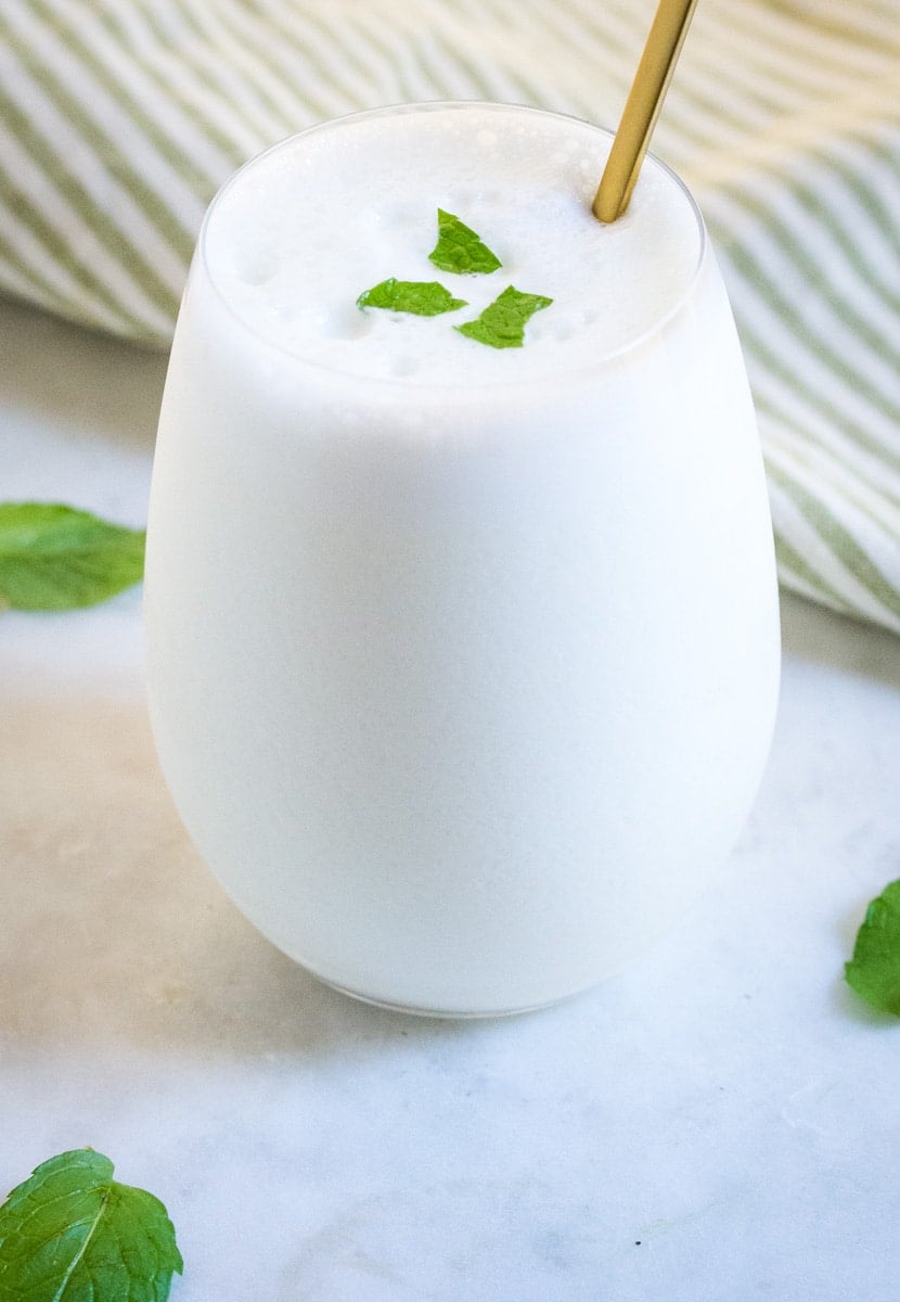 Salty lassi served in a glass goblet topped with chopped mint leaves.