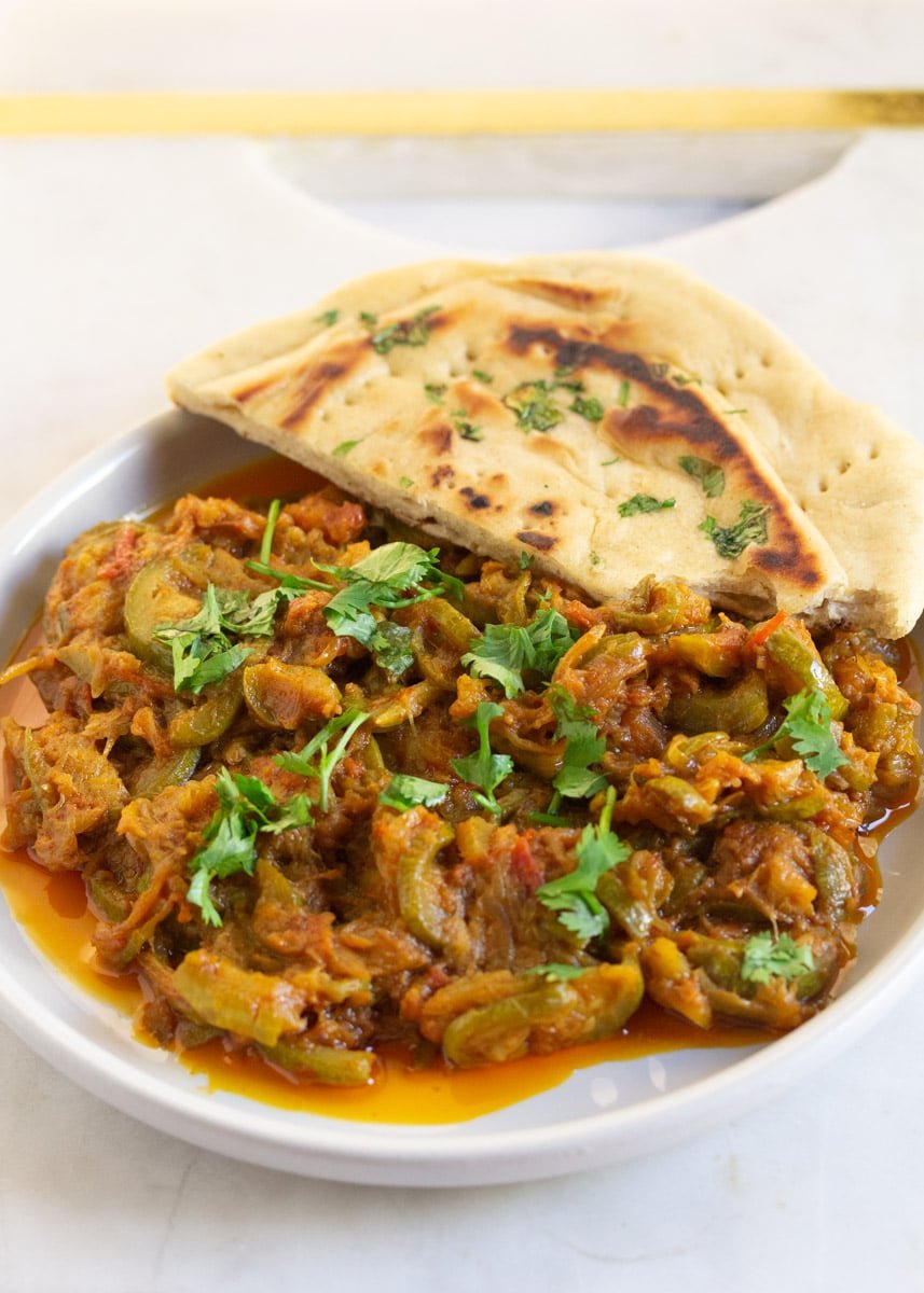 Pakistani Zucchini Curry served on a white plate with a side of naan.