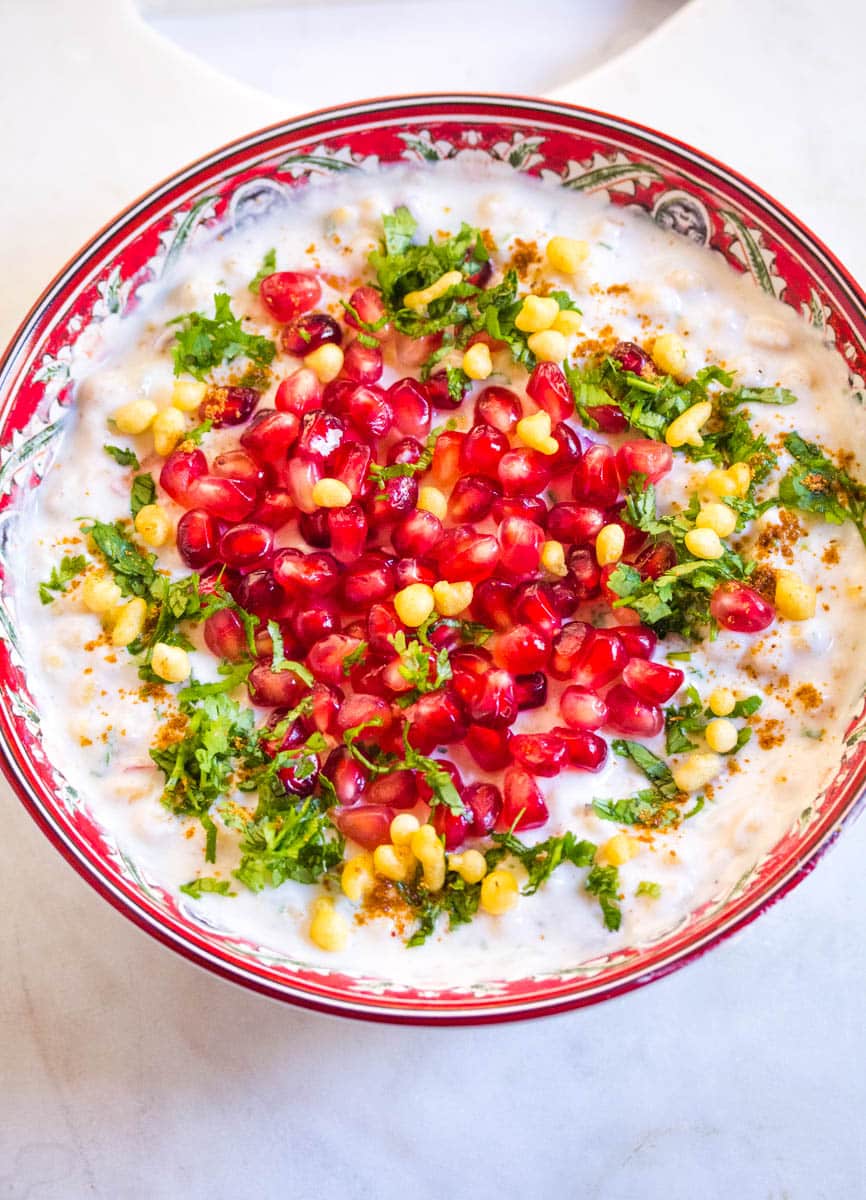 Boondi raita topped with pomegranate seeds and chopped cilantro, served in a decorative dish. 