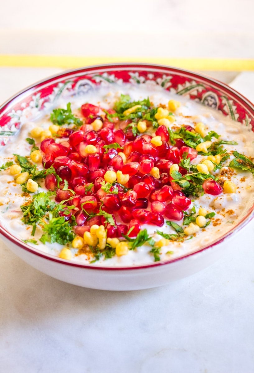 Boondi raita served in a red and white decorative bowl, topped with coriander and pomegranate. 