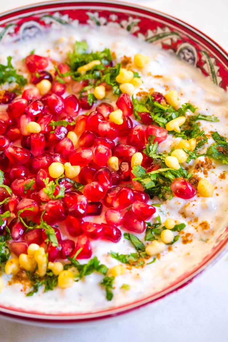 Close up view of dahi boondi raita served in a red patterned bowl. 